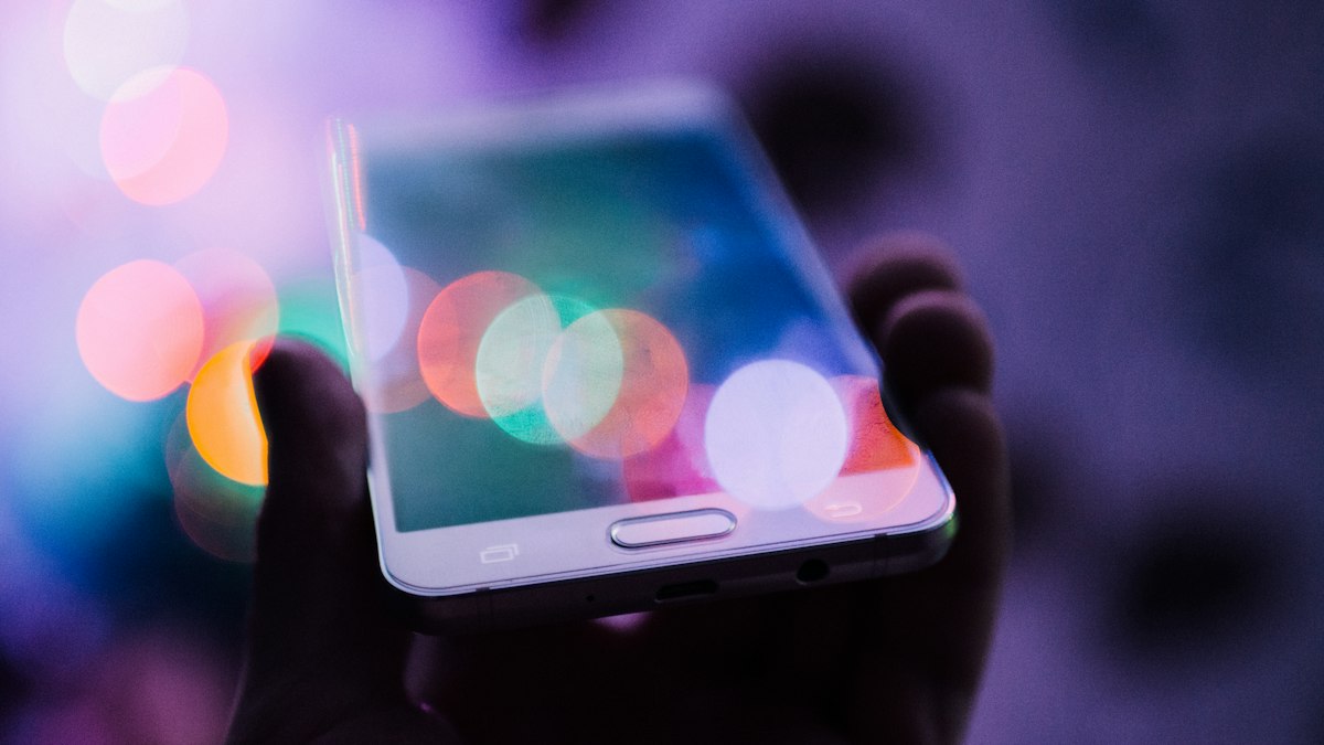 A hand holding a smartphone against coloured lights, an app in use | GPT-6