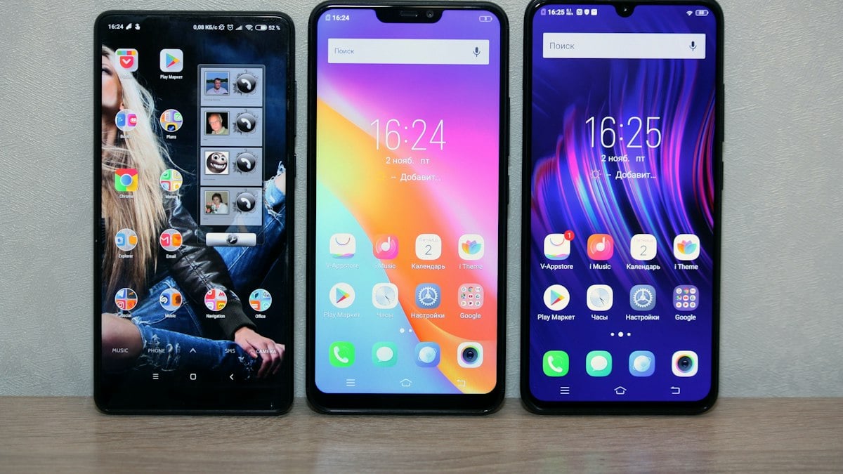 Three Android smartphones on a shelf showing home screens full of apps | Gemini 4