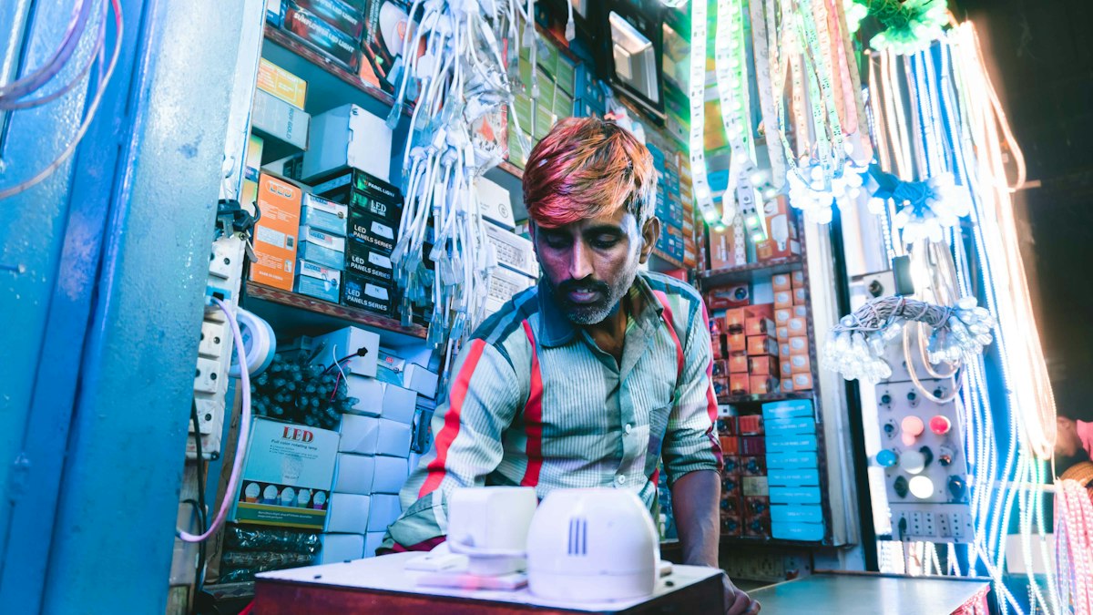 A shopkeeper at an electronics stall in India surrounded by cables, lights and boxed goods | Epic Games