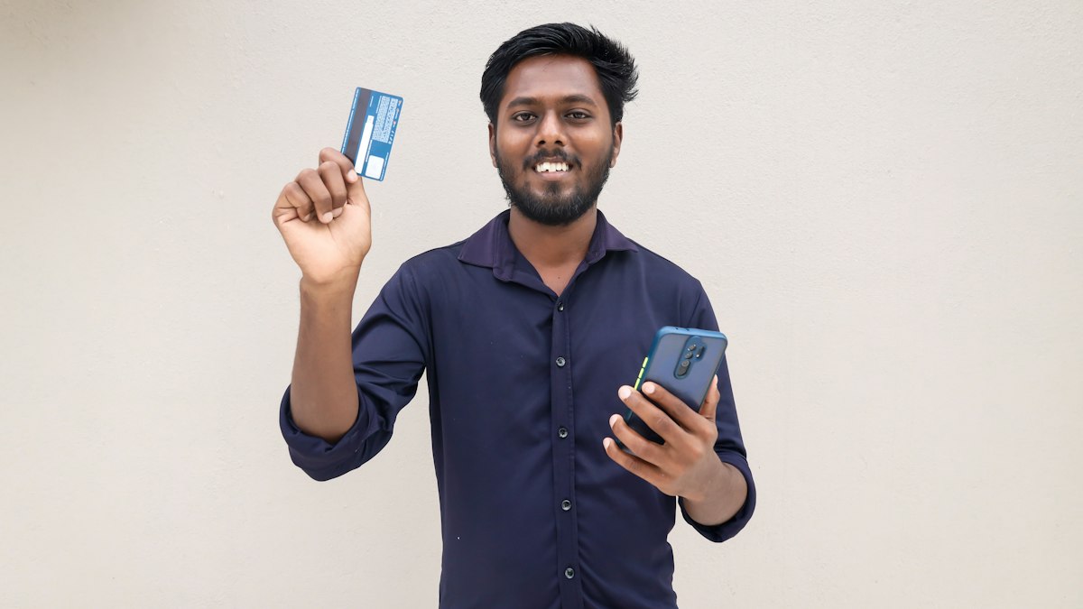 A young Indian man holding up a bank card in one hand and a smartphone in the other | Diwali 2026