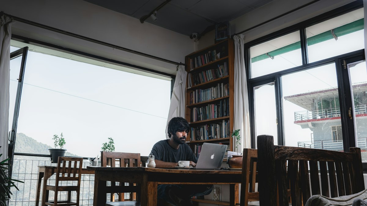 A developer working on a laptop at a long wooden table by large windows | Claude Haiku 5.5